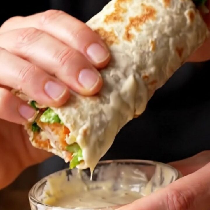 Golden toasted chicken Caesar wrap sliced diagonally, showing layers of crispy chicken, romaine, and parmesan.
