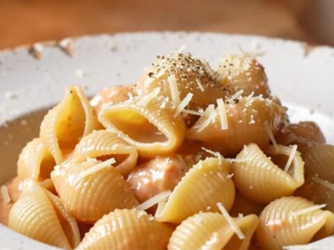 A spoon lifting a portion of creamy tomato feta shell pasta with melted cheese and basil.