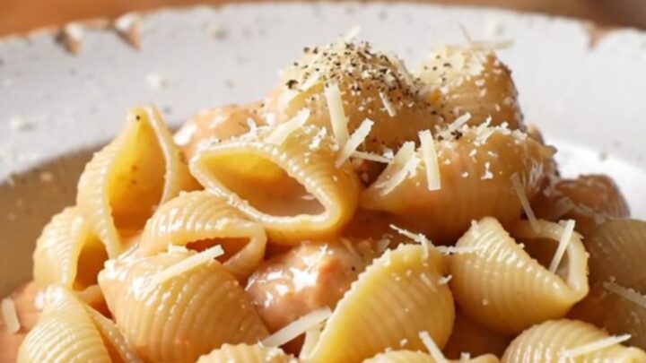 A spoon lifting a portion of creamy tomato feta shell pasta with melted cheese and basil.