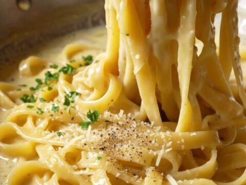 Twirled fettuccine Alfredo on a fork, coated in creamy parmesan sauce with parsley.