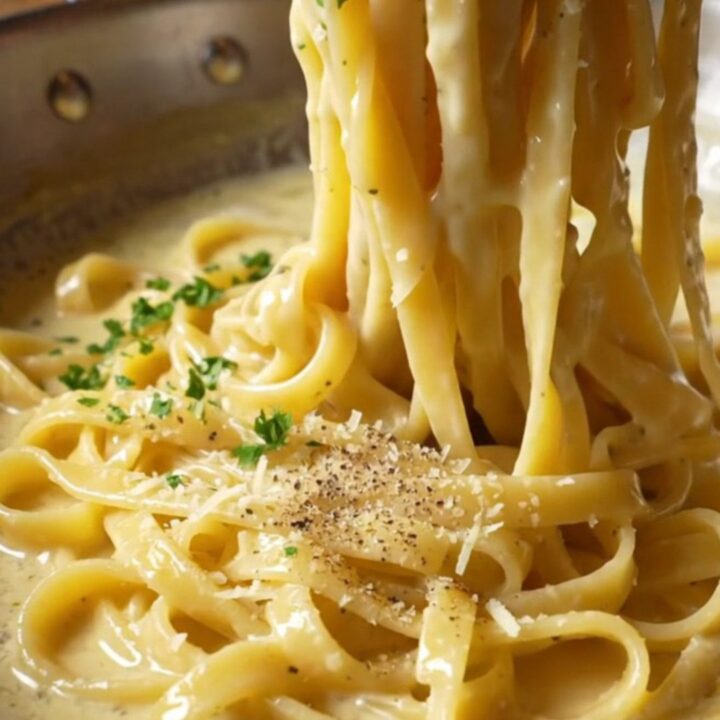 Twirled fettuccine Alfredo on a fork, coated in creamy parmesan sauce with parsley.