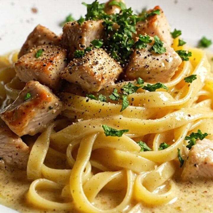 Creamy garlic parmesan chicken pasta with fettuccine, golden chicken cubes, and parsley in a white skillet