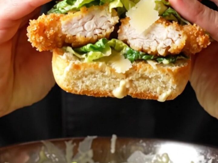 Crispy chicken Caesar sandwich on a wooden board, cut in half showing layers of chicken, romaine, and parmesan.