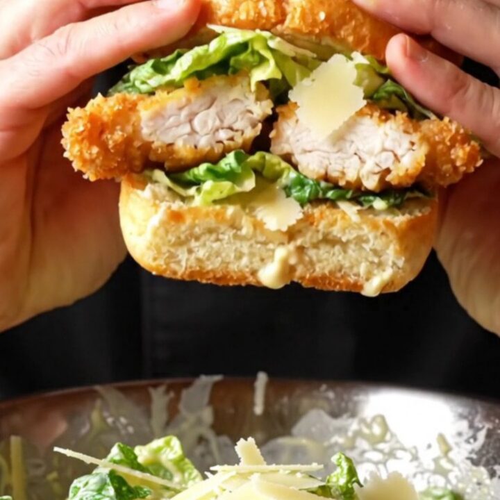 Crispy chicken Caesar sandwich on a wooden board, cut in half showing layers of chicken, romaine, and parmesan.