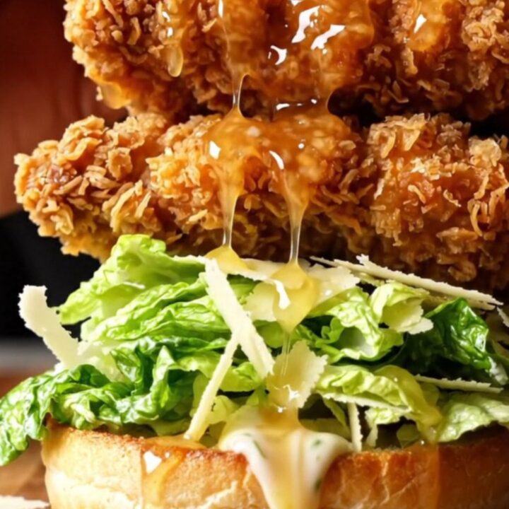 Hot honey crispy chicken Caesar sandwich on a wooden board, with honey dripping and a crunchy bite taken.