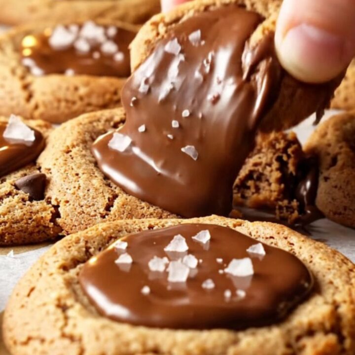 A stack of two-chip chocolate chip cookies with crispy edges and gooey centers, sprinkled with flaky sea salt.