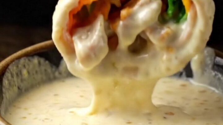 Crispy chicken shawarma wrap cut in half, showing layers of spiced chicken, fries, and pickles, with garlic sauce on the side