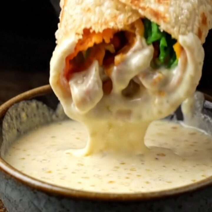 Crispy chicken shawarma wrap cut in half, showing layers of spiced chicken, fries, and pickles, with garlic sauce on the side