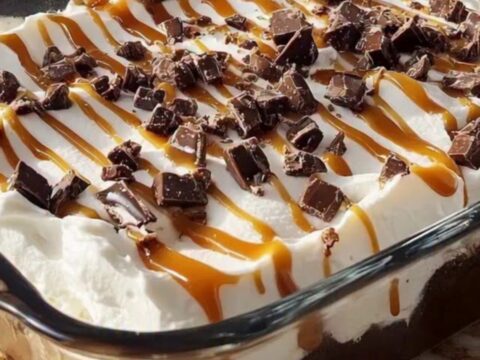 Better Than Sex Cake in a glass baking dish, whipped topping covered with caramel drizzle and chopped toffee bits on a sunlit