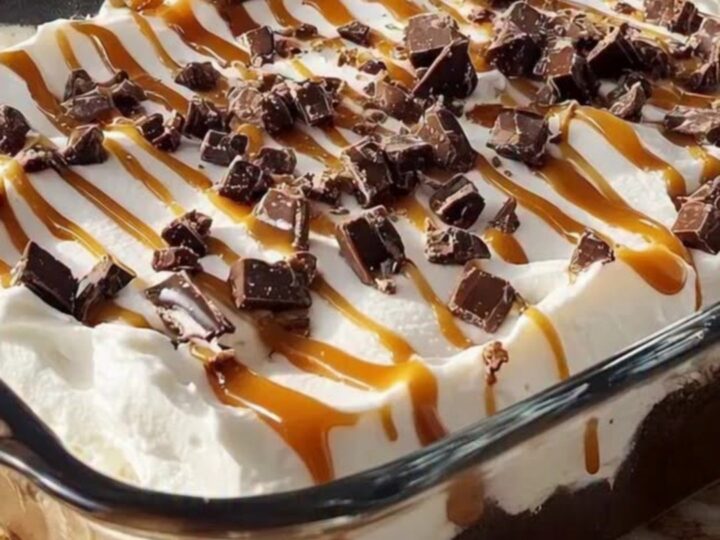 Better Than Sex Cake in a glass baking dish, whipped topping covered with caramel drizzle and chopped toffee bits on a sunlit