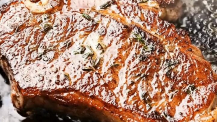 Golden-crusted cast iron ribeye steak coated in herb-garlic butter, lifted steaming from a black skillet with tongs