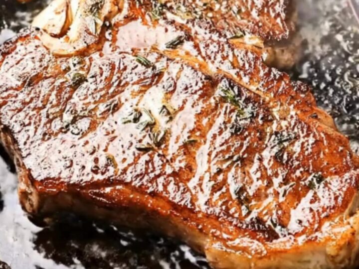 Golden-crusted cast iron ribeye steak coated in herb-garlic butter, lifted steaming from a black skillet with tongs
