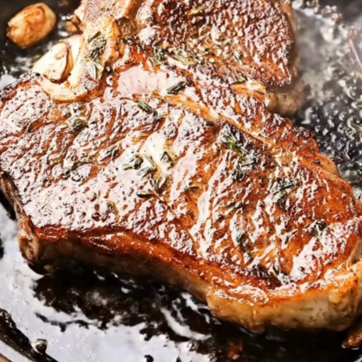 Golden-crusted cast iron ribeye steak coated in herb-garlic butter, lifted steaming from a black skillet with tongs