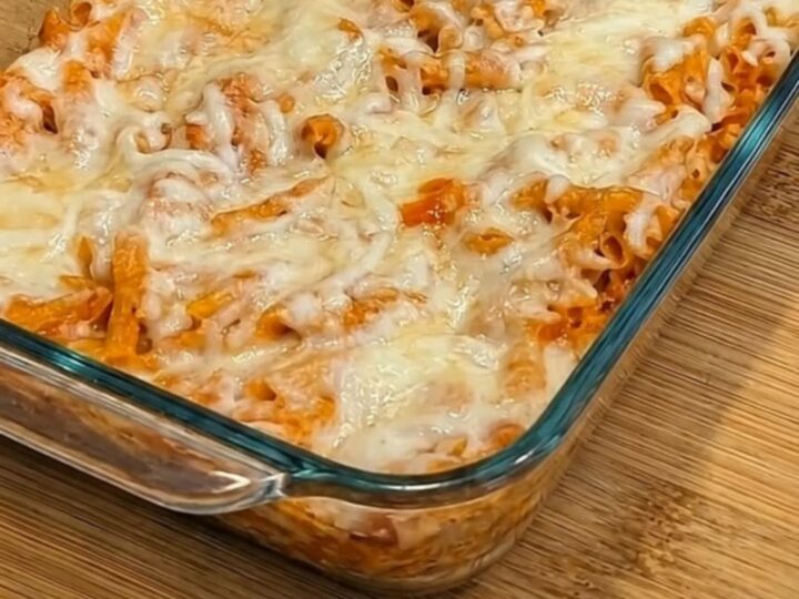 Baked chicken parmesan casserole with penne and melted mozzarella in a glass baking dish, a spatula lifting a cheesy portion