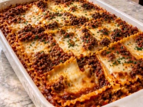 Slice of baked beef lasagna lifted from a white ceramic dish with a long stretchy cheese pull and steam rising