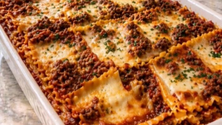 Slice of baked beef lasagna lifted from a white ceramic dish with a long stretchy cheese pull and steam rising