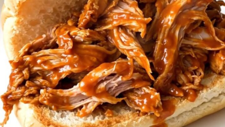 Shredded buffalo turkey tenderloin piled high on a toasted roll, glossy orange sauce dripping onto a white plate