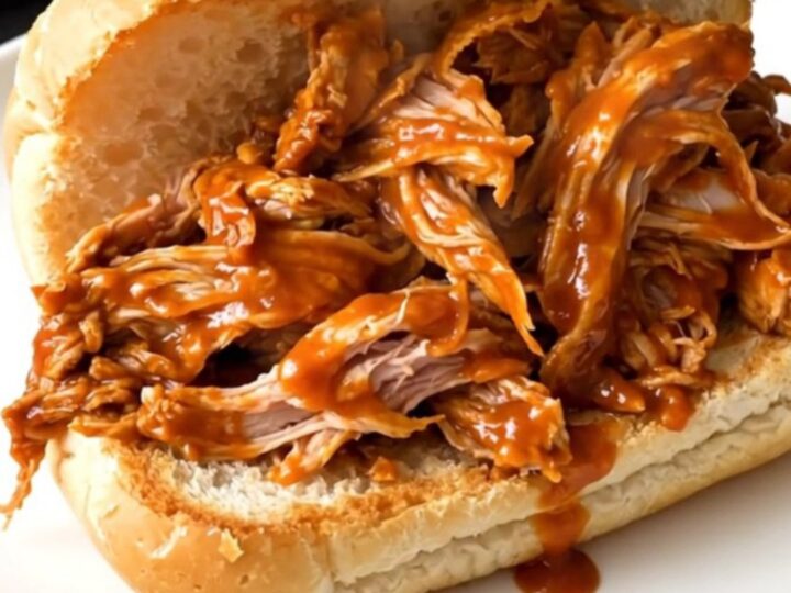 Shredded buffalo turkey tenderloin piled high on a toasted roll, glossy orange sauce dripping onto a white plate