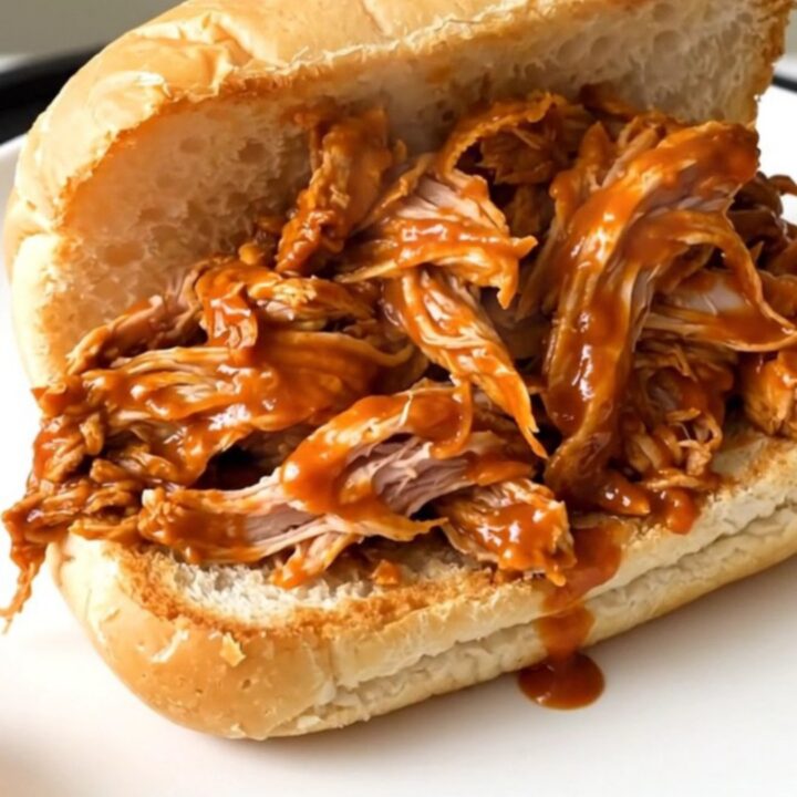 Shredded buffalo turkey tenderloin piled high on a toasted roll, glossy orange sauce dripping onto a white plate