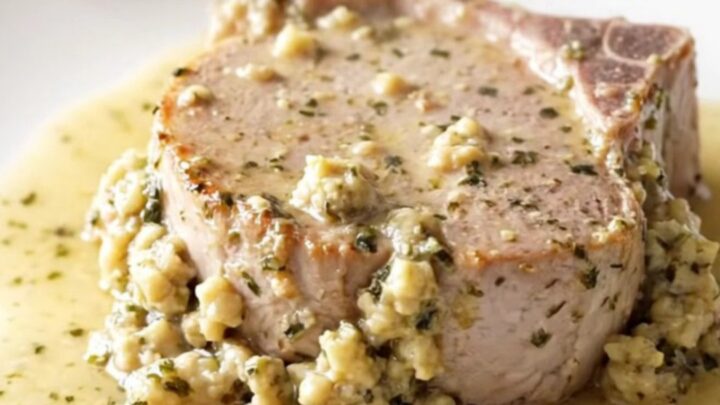 Boneless pork chop topped with creamy herb stuffing on a white plate, thick sauce and steam rising