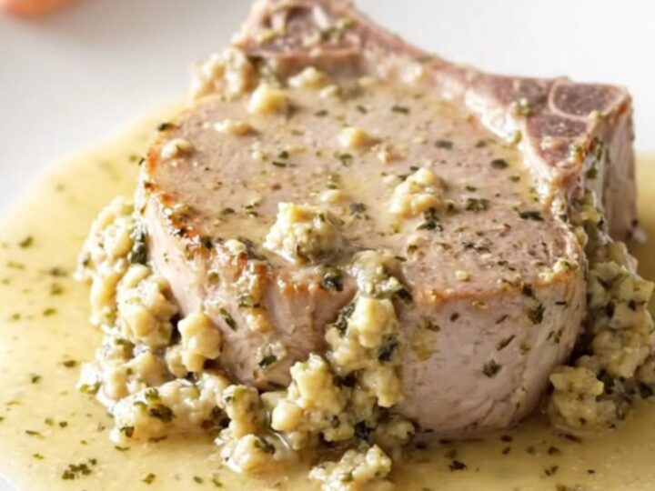 Boneless pork chop topped with creamy herb stuffing on a white plate, thick sauce and steam rising