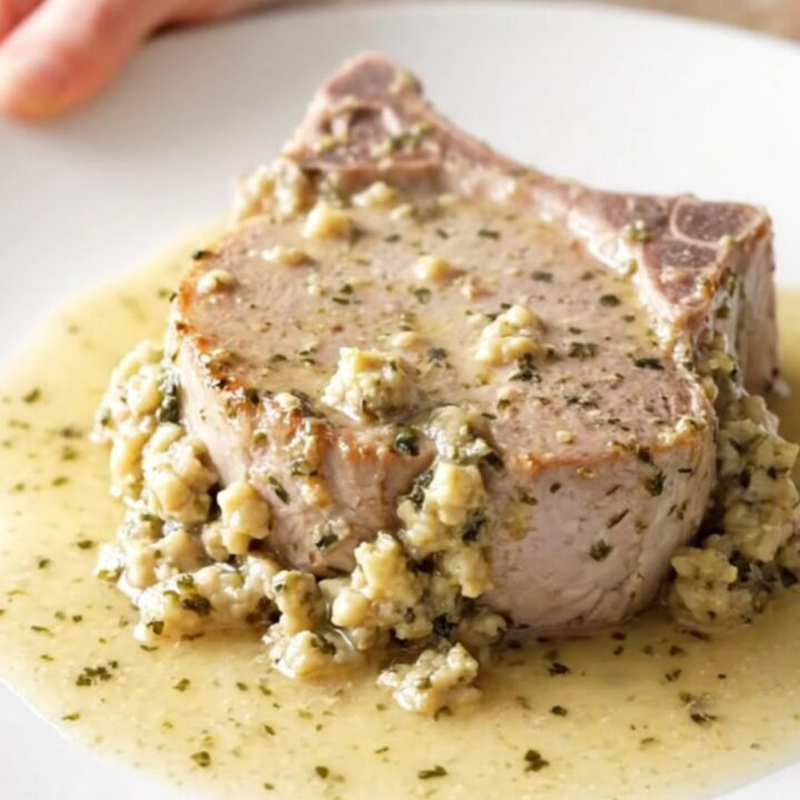 Boneless pork chop topped with creamy herb stuffing on a white plate, thick sauce and steam rising