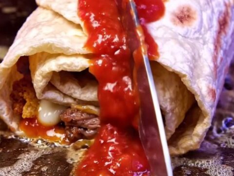 Crispy carne asada burrito cut in half showing molten nacho cheese and a vivid red crushed chip core