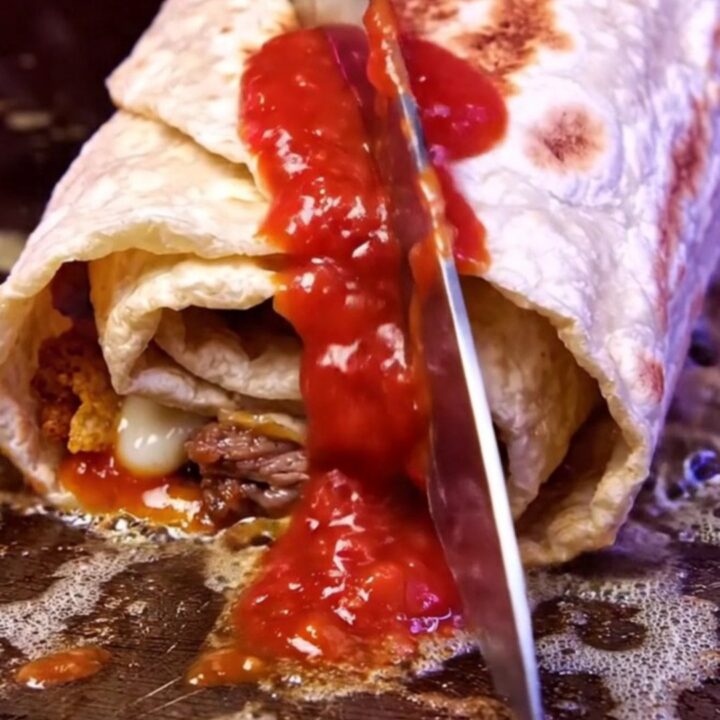 Crispy carne asada burrito cut in half showing molten nacho cheese and a vivid red crushed chip core
