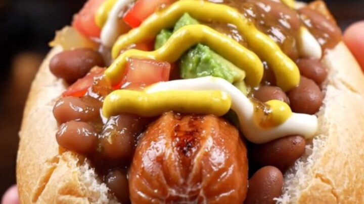 Bacon-wrapped Sonoran hot dog in a steamed bolillo loaded with pinto beans, caramelized onions, diced tomatoes