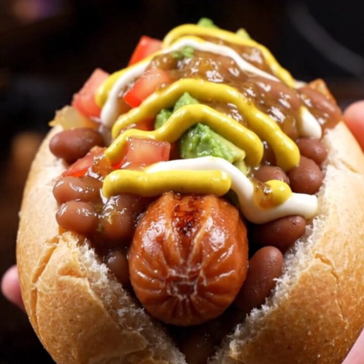 Bacon-wrapped Sonoran hot dog in a steamed bolillo loaded with pinto beans, caramelized onions, diced tomatoes