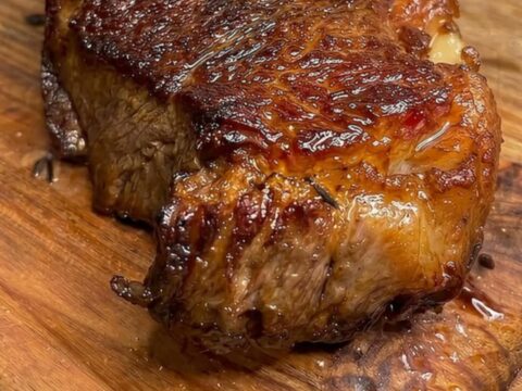 Golden-brown pan-seared ribeye steak on a wooden cutting board, sliced to show a juicy pink center with steam rising