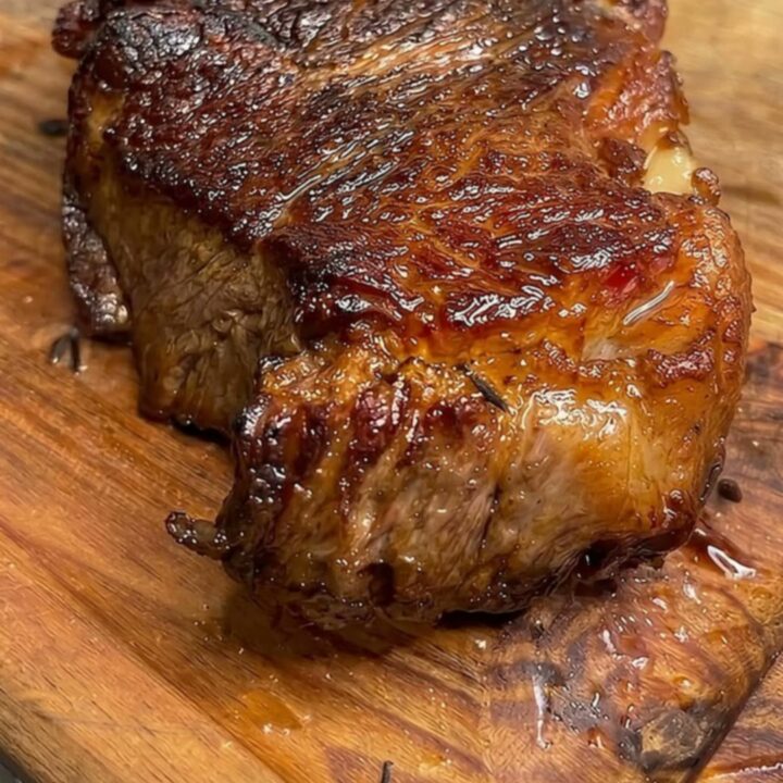 Golden-brown pan-seared ribeye steak on a wooden cutting board, sliced to show a juicy pink center with steam rising