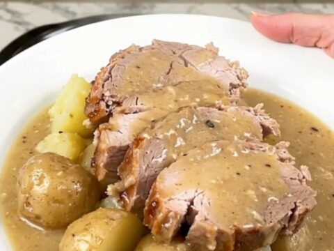 Slices of crockpot pork loin with soft baby potatoes under thick creamy bacon gravy on a white plate