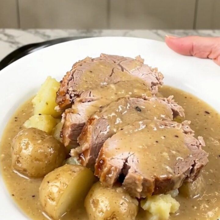 Slices of crockpot pork loin with soft baby potatoes under thick creamy bacon gravy on a white plate