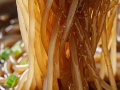 Translucent glass noodles in dark truffle soy glaze topped with scallions and shaved black truffle in a dark bowl