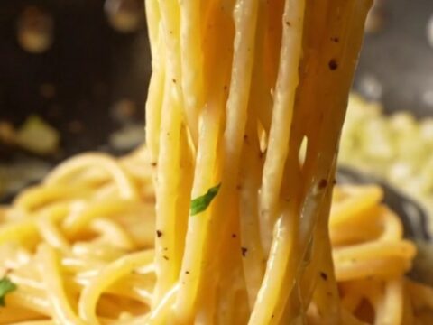 A fork twirling creamy lemon garlic spaghetti with a glossy sauce, parsley, and cracked black pepper.