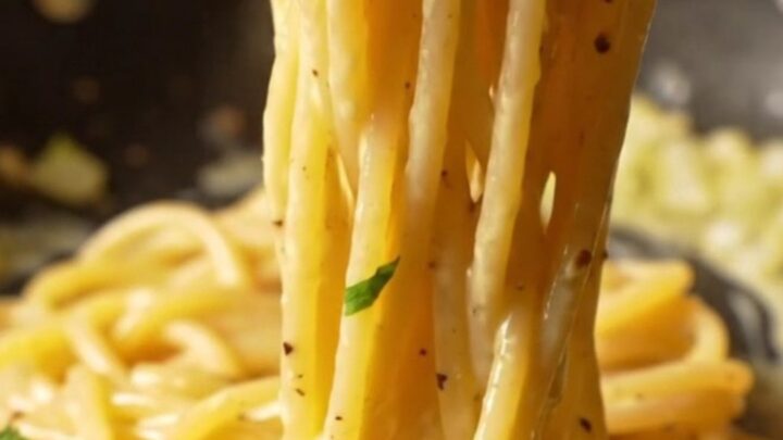 A fork twirling creamy lemon garlic spaghetti with a glossy sauce, parsley, and cracked black pepper.