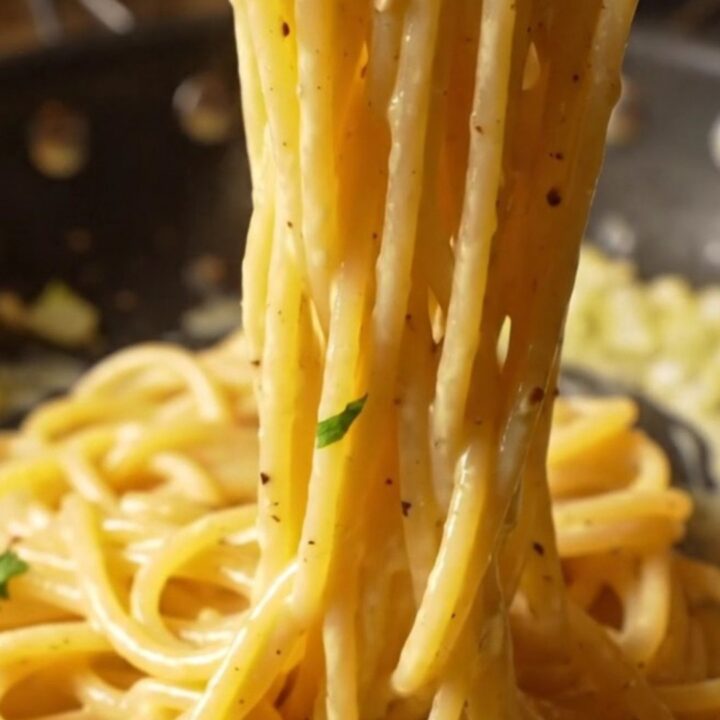 A fork twirling creamy lemon garlic spaghetti with a glossy sauce, parsley, and cracked black pepper.