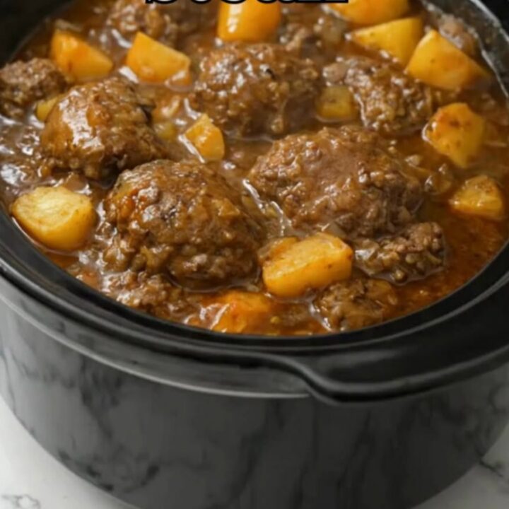A serving spoon lifting a tender Salisbury steak patty and potato chunks in steaming onion gravy from a black slow cooker
