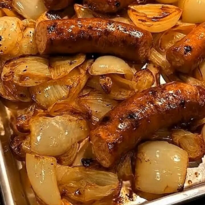 Golden roasted sausages and caramelized sweet onion wedges steaming on a sheet pan