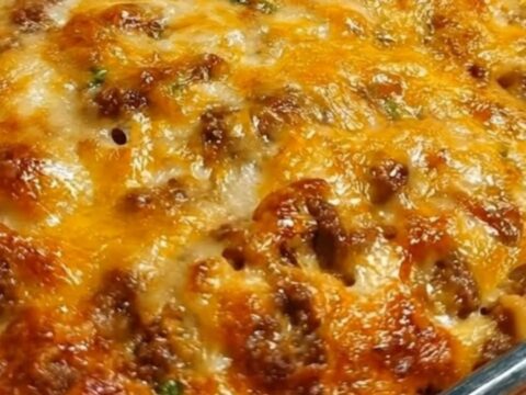 Golden baked spaghetti in a glass dish with a spatula lifting a cheesy slice and a long mozzarella pull