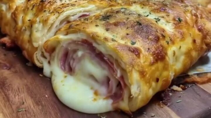 Golden sliced Italian stromboli on a wooden cutting board with a slice lifted in a long stretchy mozzarella pull
