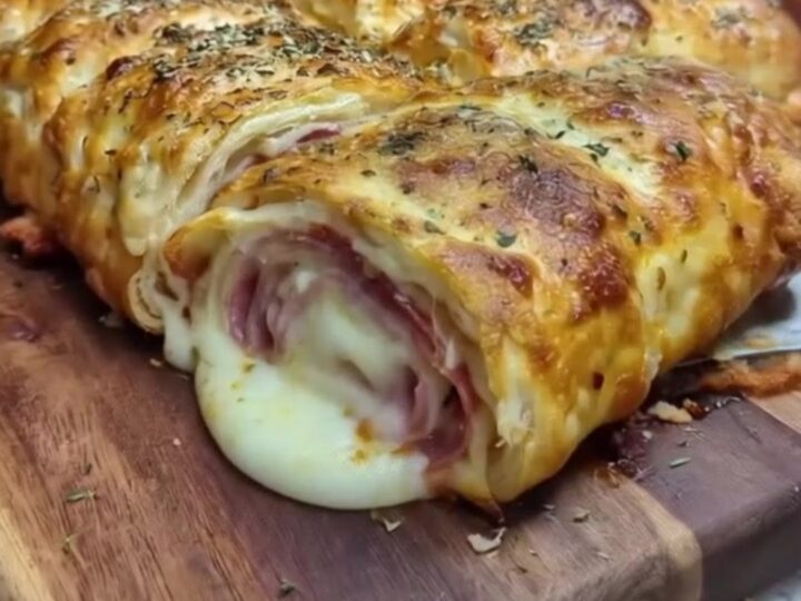 Golden sliced Italian stromboli on a wooden cutting board with a slice lifted in a long stretchy mozzarella pull