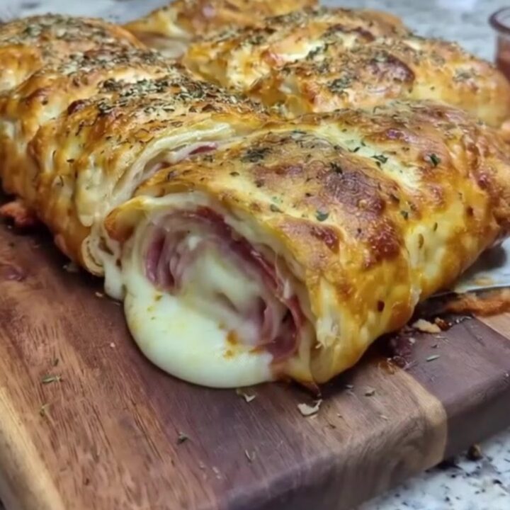 Golden sliced Italian stromboli on a wooden cutting board with a slice lifted in a long stretchy mozzarella pull