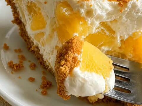 Thick slice of no-bake pineapple cream cheesecake on a white plate, creamy filling with pineapple chunks and cookie crust