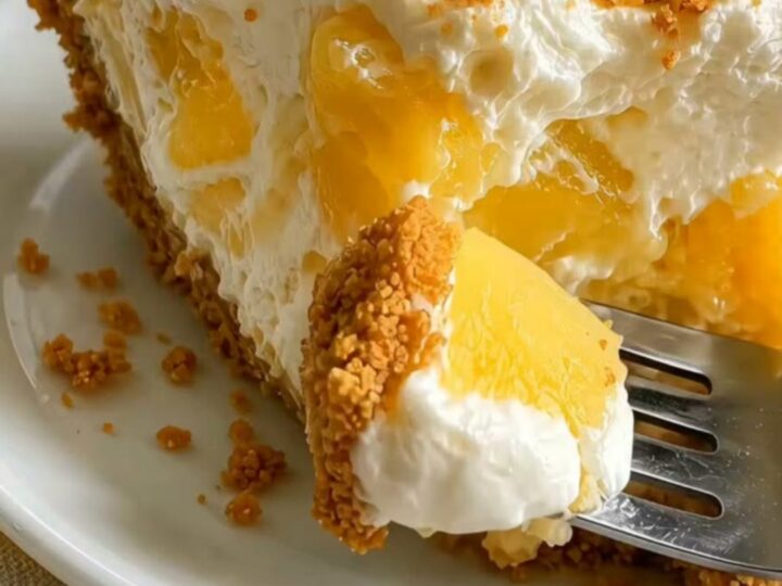 Thick slice of no-bake pineapple cream cheesecake on a white plate, creamy filling with pineapple chunks and cookie crust