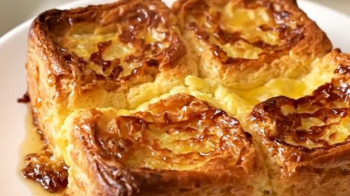 Golden puffed crockpot French toast casserole steaming on a white plate against cream kitchen cabinets