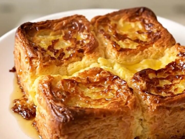 Golden puffed crockpot French toast casserole steaming on a white plate against cream kitchen cabinets