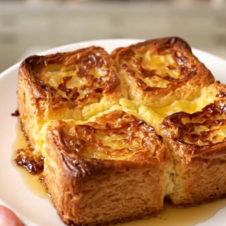 Golden puffed crockpot French toast casserole steaming on a white plate against cream kitchen cabinets