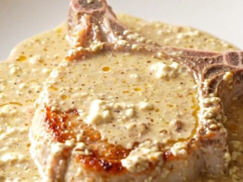 Boneless pork chop smothered in thick creamy cheddar sauce on a white plate, steam rising in a bright kitchen